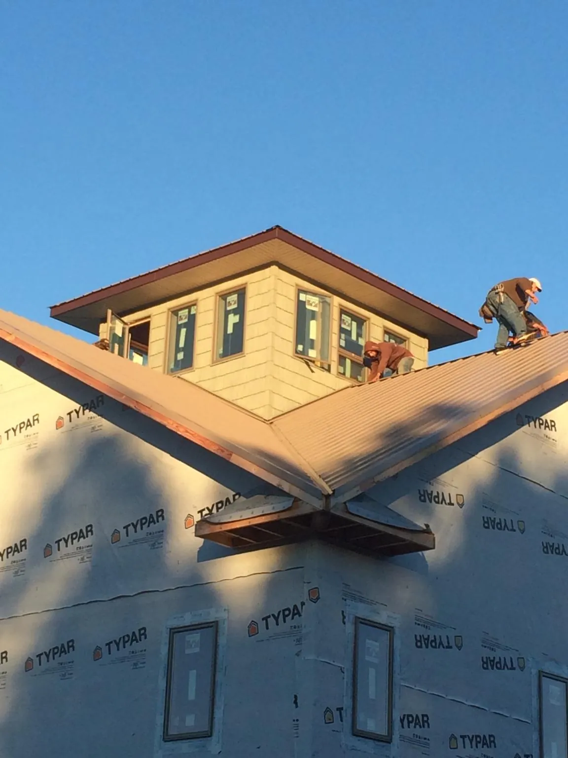 Roofers working around a rooftop cupola on a new metal roof at sunset — Roof Waterproofing in Huron by Roofing Brothers